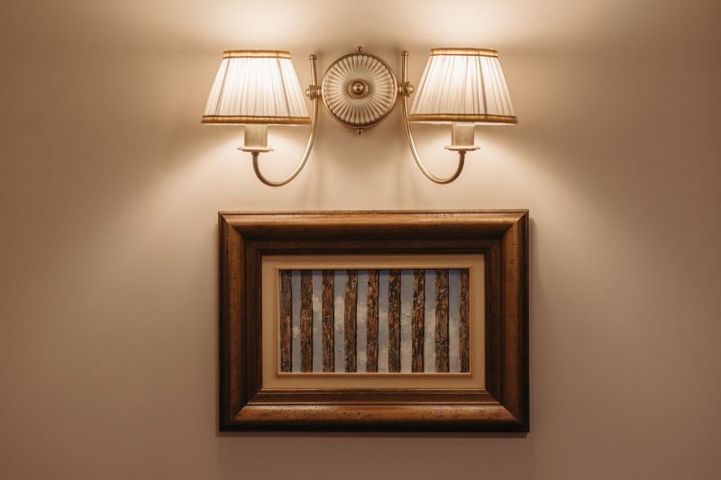 Framed abstract painting hanging beneath a warm brass wall lamp on a softly lit wall