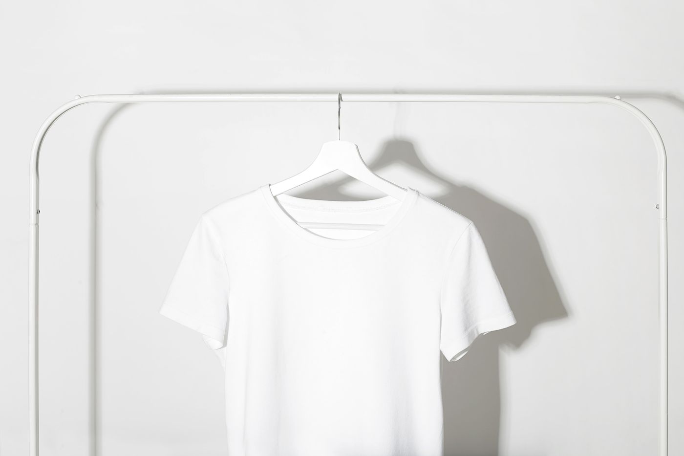 A plain cotton tee on a rail against a bare white wall