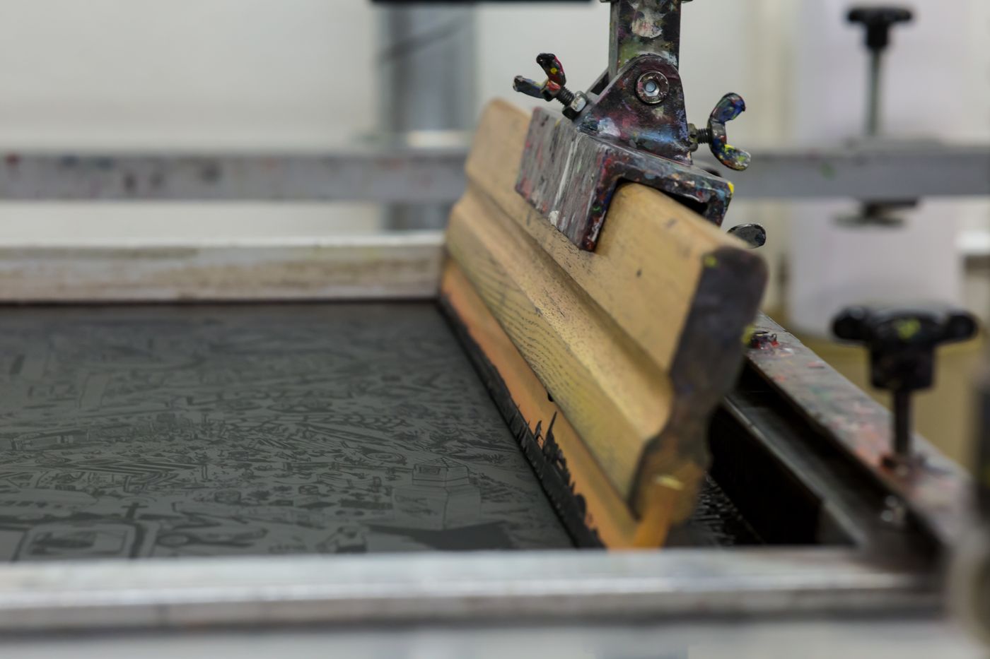 A wooden squeegee resting on an exposed screen in a studio