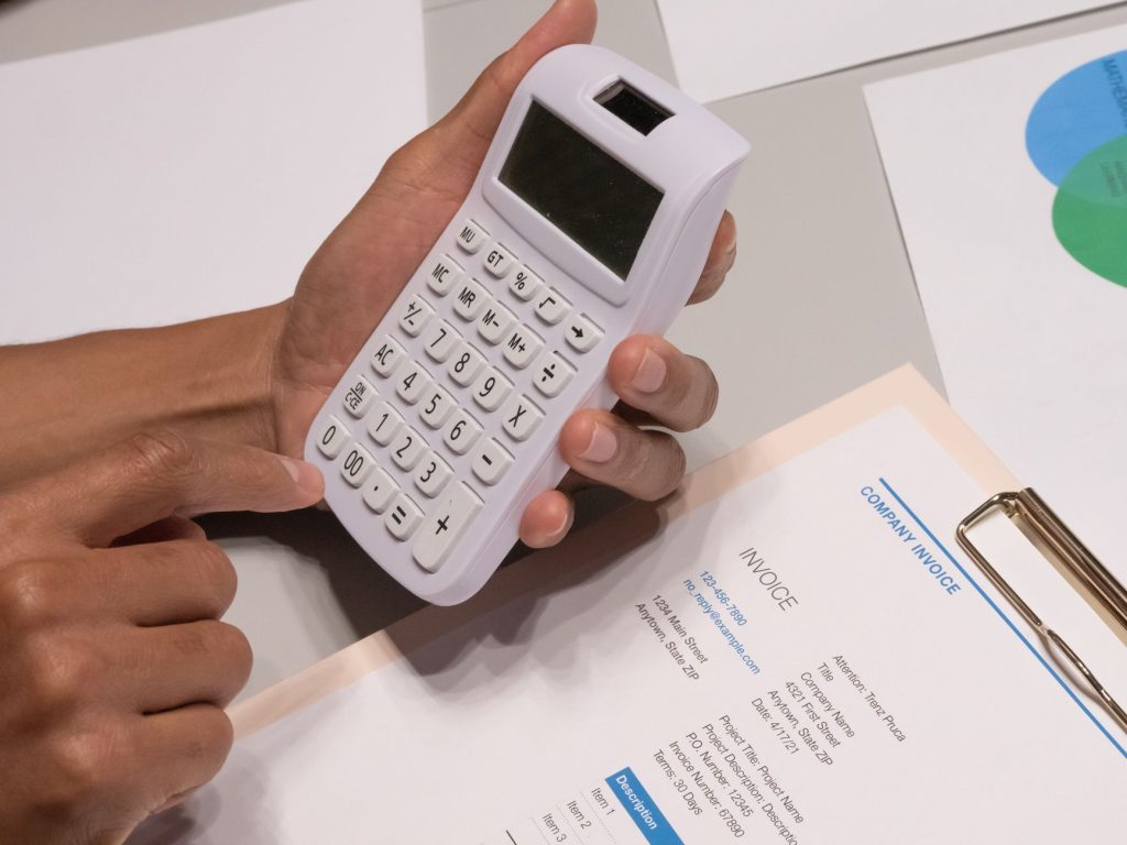A hand holding a calculator over a printed invoice