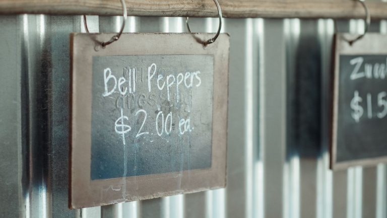 A handwritten chalkboard price sign hanging on corrugated metal