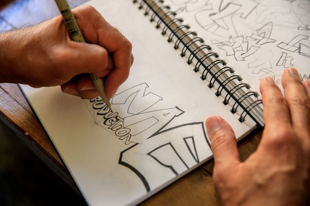 A hand sketching lettering in a spiral notebook