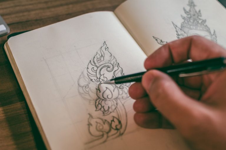 A hand sketching a detailed design in a sketchbook with a mechanical pencil
