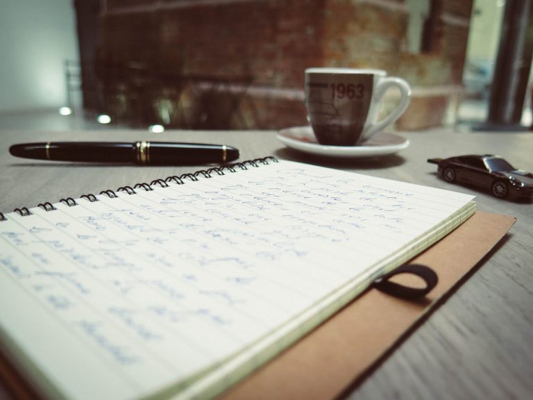 A notebook, pen and coffee cup on a desk