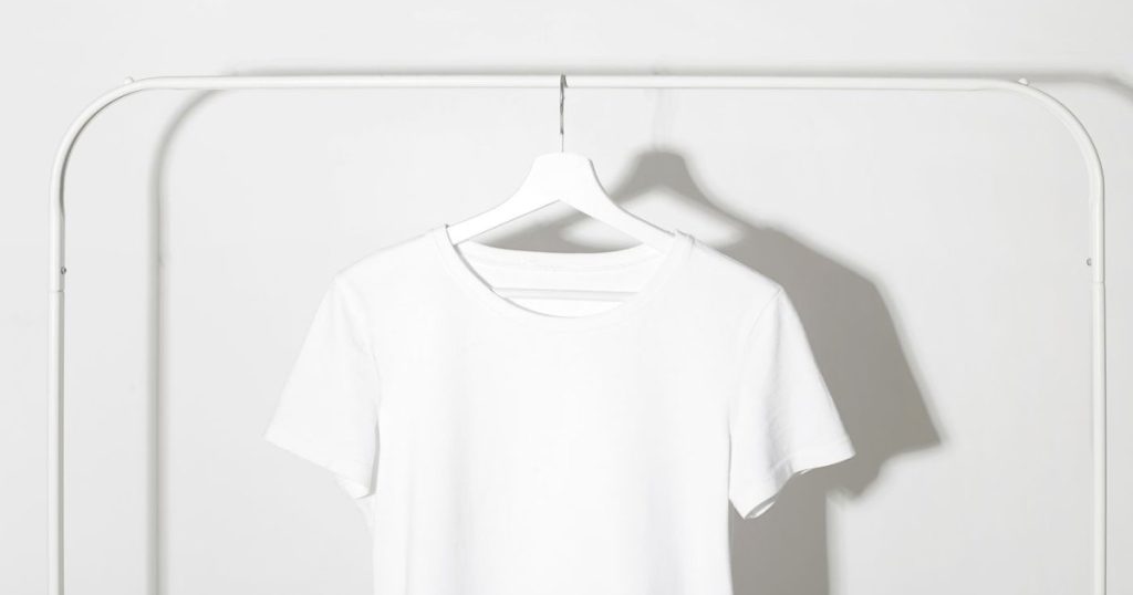 A plain cotton tee on a rail against a bare white wall