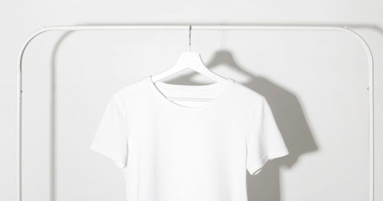 A plain cotton tee on a rail against a bare white wall