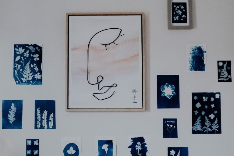 Small blue cyanotype prints and a framed line drawing arranged on a pale wall