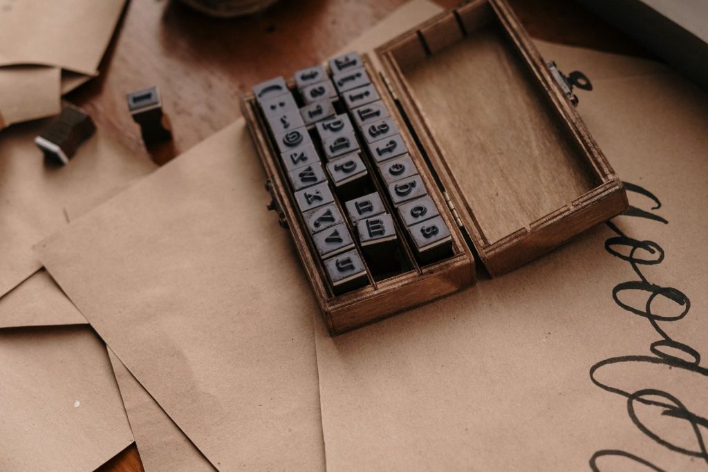 Open wooden case of rubber stamps on brown kraft paper with calligraphy flourishes