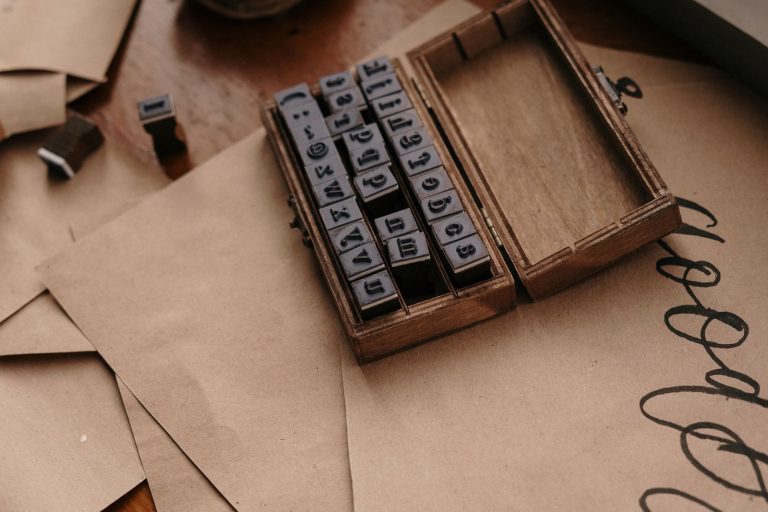 Open wooden case of rubber stamps on brown kraft paper with calligraphy flourishes